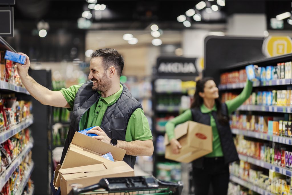 The employees putting groceries on aisle and exposing them at supermarket.