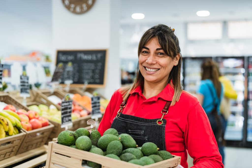 Woman working in supermarket holding a box containing fresh avocados